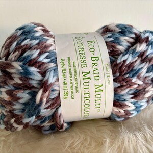 K&ouml;nnte beinhalten: Eine blaue, wei&szlig;e und braune Garnrolle mit der Aufschrift "Eco-Braid Multi&trade; &Eacute;co-Tressee Multicolore", hergestellt aus recyceltem Kunststoff. Das Garn ist 44 Yards/8,8 oz oder 40 m/250 g.