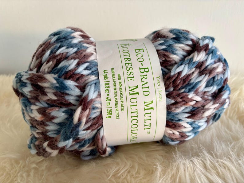 K&ouml;nnte beinhalten: Eine blaue, wei&szlig;e und braune Garnrolle mit der Aufschrift "Eco-Braid Multi&trade; &Eacute;co-Tressee Multicolore", hergestellt aus recyceltem Kunststoff. Das Garn ist 44 Yards/8,8 oz oder 40 m/250 g.