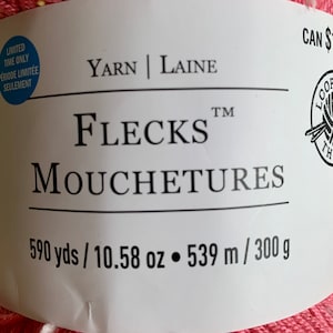 Puede incluir: Una madeja de hilo rosa con motas blancas. La etiqueta dice "Yarn | Laine", "FlecksTM", "Mouchetures", "590 yds / 10.58 oz", "539 m / 300 g" y "CAN $11.99".