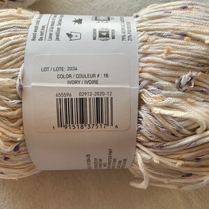 Peut inclure: Une pelote de fil ivoire avec un motif mouchet&eacute; blanc et violet. L'&eacute;tiquette du fil comprend le num&eacute;ro de lot 2034, le num&eacute;ro de couleur 16 et la composition du fil : 79 % acrylique et 21 % polyester.