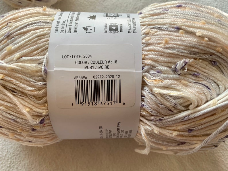 Peut inclure: Une pelote de fil ivoire avec un motif mouchet&eacute; blanc et violet. L'&eacute;tiquette du fil comprend le num&eacute;ro de lot 2034, le num&eacute;ro de couleur 16 et la composition du fil : 79 % acrylique et 21 % polyester.