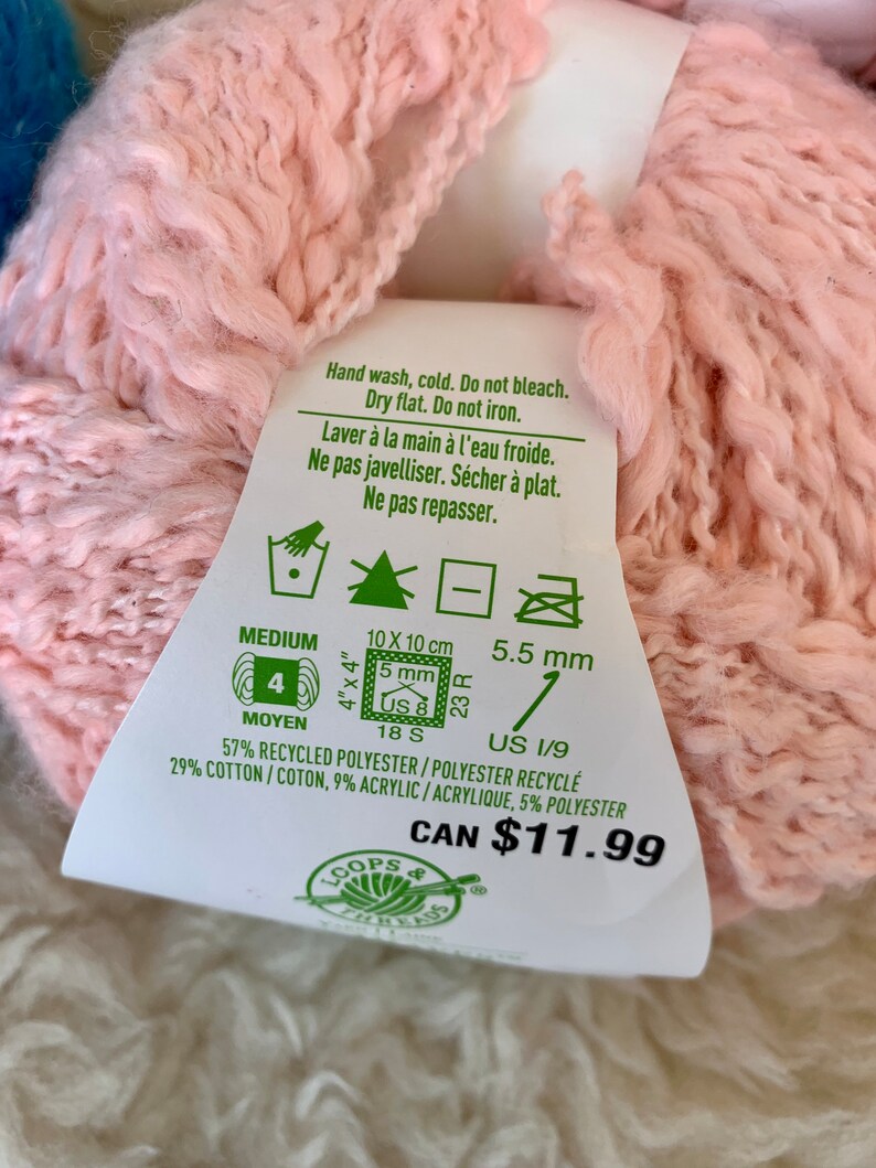 May include: A pink yarn ball with a white label that says "Hand wash, cold. Do not bleach. Dry flat. Do not iron." and "57% Recycled Polyester / Polyester Recycl&eacute; 29% Cotton / Coton, 9% Acrylic /Acrylique, 5% Polyester" and "CAN $11.99".