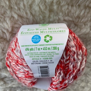 May include: A skein of red and cream yarn labeled "Eco-Waves Multi" with the text "496 yds / 7 oz. 453 m / 200 g" and "Color / Couleur # 09 Red Cream / Creme Rouge".