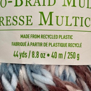 K&ouml;nnte beinhalten: Eine Kn&auml;uel dickes, mehrfarbiges Garn in Blaut&ouml;nen, Wei&szlig; und Braun. Das Garn besteht aus recyceltem Kunststoff und ist mit "O-BRAID MULTRESSE MULTIC" und dem Text "MADE FROM RECYCLED PLASTIC FABRIQU&Eacute; &Agrave; PARTIR DE PLASTIQUE RECYCL&Eacute; 44 yds / 8.8 oz &bull; 40 m / 250 g" beschriftet.