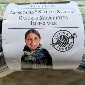 Puede incluir: Una madeja de hilo con un patrón moteado blanco, verde y negro. La etiqueta del hilo dice "IMPECCABLE® SPECKLE STRIPES™ RAYURES MOUCHETÉES IMPECCABLE" y presenta a una mujer usando una bufanda hecha con el hilo. La etiqueta también incluye el logotipo de Loops & Threads.