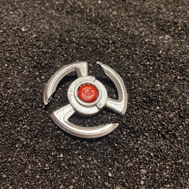 May include: A silver-colored metal toy with three arms and a red center. The toy is on a black background.