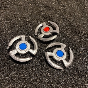 May include: Three silver metal spinners with different colored centers. The first spinner has a red center, the second has a blue center, and the third has a blue center.