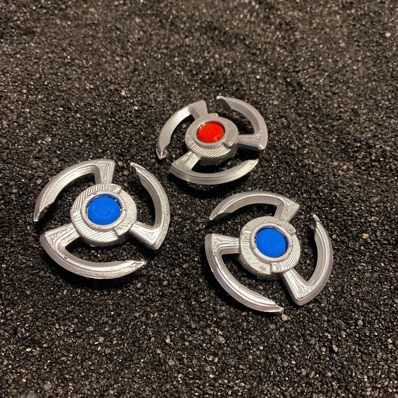 May include: Three silver metal spinners with different colored centers. The first spinner has a red center, the second has a blue center, and the third has a blue center.