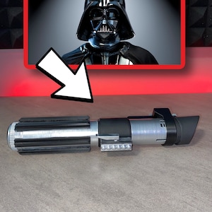 May include: A silver and black lightsaber prop with a rectangular emitter and a series of small lights. The image also features a framed picture of Darth Vader. The lightsaber is a replica of the one used by Darth Vader.