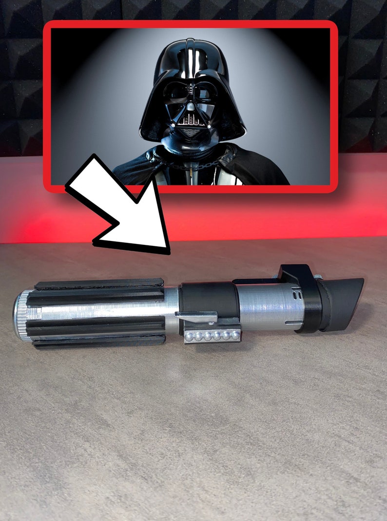 May include: A silver and black lightsaber prop with a rectangular emitter and a series of small lights. The image also features a framed picture of Darth Vader. The lightsaber is a replica of the one used by Darth Vader.