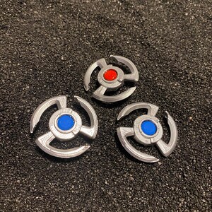May include: Three silver metal star-shaped objects with a central circle. The top object has a red circle in the center, the left object has a blue circle in the center, and the right object has a blue circle in the center.