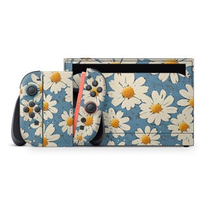 May include: A Nintendo Switch console and controllers with a daisy floral pattern. The design features large white daisies with yellow centers on a light blue background. The controllers have black accents and orange rails.
