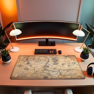 Puede incluir: Una configuración de escritorio con un monitor curvo, teclado y ratón. Una alfombrilla de ratón rectangular grande con un diseño de mapa vintage es el punto focal. Dos lámparas de escritorio y plantas en macetas flanquean el monitor. Hay auriculares a la derecha.