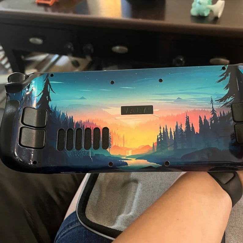 May include: A black and blue video game console with a colorful landscape design. The console has a black "VALVE" logo on the front.