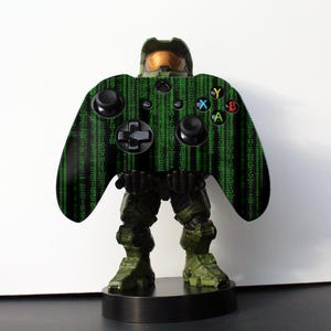 Op de afbeelding: Een groene en zwarte Xbox-controller met een Master Chief-ontwerp. De controller staat op een zwarte basis.