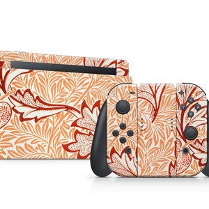 Op de afbeelding: Een Switch-console en controllers met een decoratieve skin met een bloemmotief in tinten oranje en rood op een crèmekleurige achtergrond. De controllers hebben zwarte accenten en knoppen.