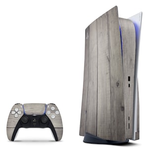 May include: A white and gray PlayStation 5 console with a wood-grain design. The console is open, revealing the disc drive. A matching wood-grain controller is also shown.