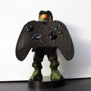 K&ouml;nnte beinhalten: Ein schwarzer und gr&uuml;ner Videospiel-Controller mit goldenem Design. Der Controller ist in Form eines Master Chief aus der Halo-Videospielserie gestaltet.