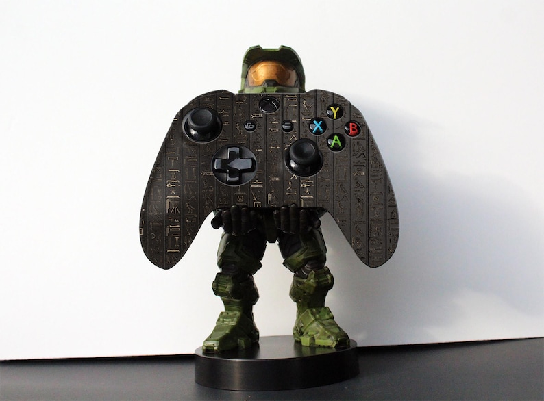 K&ouml;nnte beinhalten: Ein schwarzer und gr&uuml;ner Videospiel-Controller mit goldenem Design. Der Controller ist in Form eines Master Chief aus der Halo-Videospielserie gestaltet.