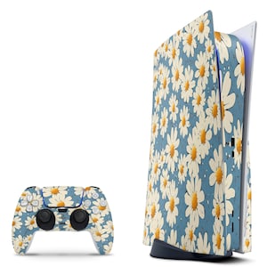 May include: A gaming console and controller set featuring a daisy floral pattern. The console is white with a blue and white daisy design on the side panels. The controller has the same daisy pattern. The background is white.