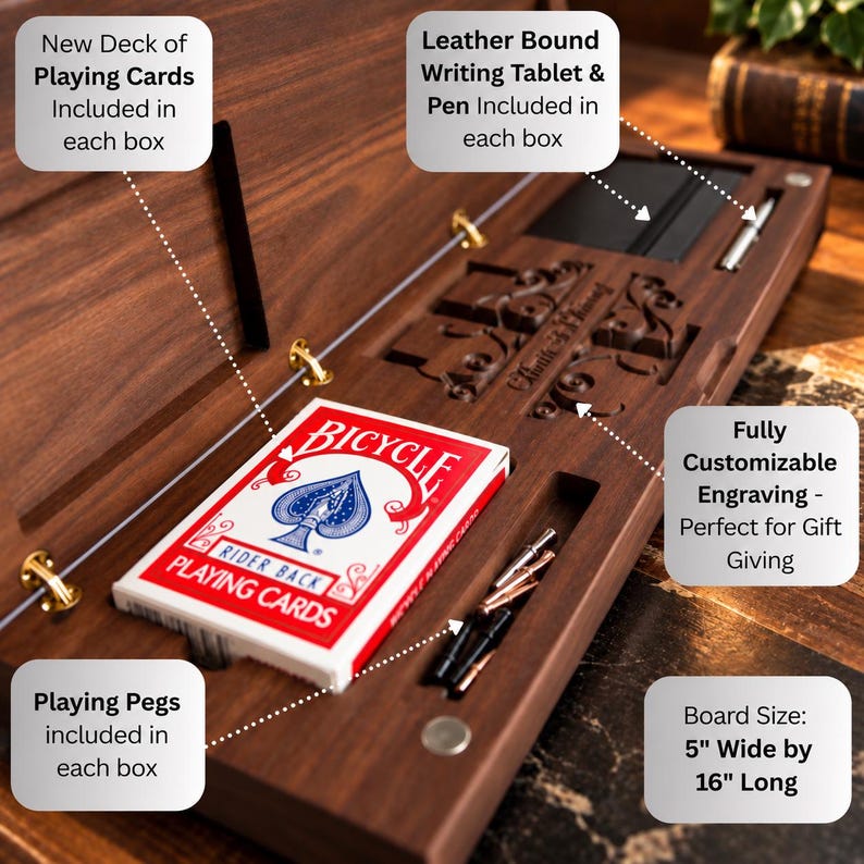 May include: A dark wood cribbage board measuring 12.7 cm wide by 40.64 cm long, featuring a deck of Bicycle playing cards, a leather-bound writing tablet, a pen, and metal playing pegs. The board includes an area for customizable engraving.