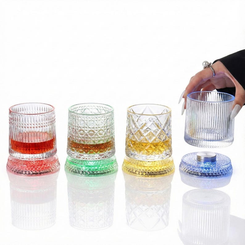 May include: Set of four decorative drinking glasses with colored bases. The glasses have different patterns and contain liquids of varying colors. One glass is being held by a person.