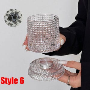 May include: A clear, textured glass container with a matching lid. The container has a diamond pattern, and the lid has a silver center. The text "Style 6" is visible in the lower left corner. A small, round adhesive pad is in the upper left.