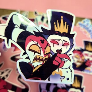 May include: Holographic sticker featuring two cartoon characters in a close embrace. One character has red skin, yellow eyes, and a black and white striped hat. The other character has blue skin and a gold crown. The sticker has a pink background.