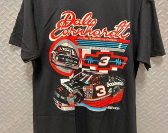 Può includere: Maglietta nera con un'immagine colorata della macchina da corsa di Dale Earnhardt. La macchina è il numero 3 e ha il testo "Dale Earnhardt" e "Five Time Winston Cup Champion".