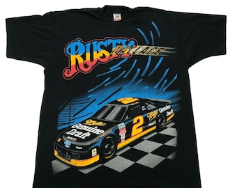 May include: Black t-shirt with a graphic of race car driver Rusty Wallace in a blue and yellow Miller Genuine Draft car. The car is number 2 and is on a checkered flag background.