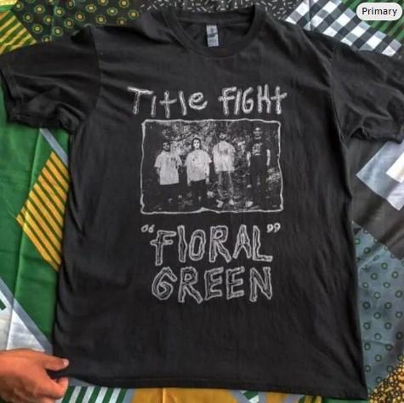May include: Black t-shirt with the band name "Title Fight" in white, above a grayscale image of the band members. Below the image, the words "Floral Green" are printed in white, within quotation marks. The shirt is made of a soft material.