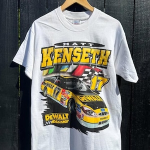 May include: White t-shirt with a yellow and black race car graphic. The car has the number 17 and the text "DEWALT RACING" on it. The text "MATT KENSETH" is above the car.