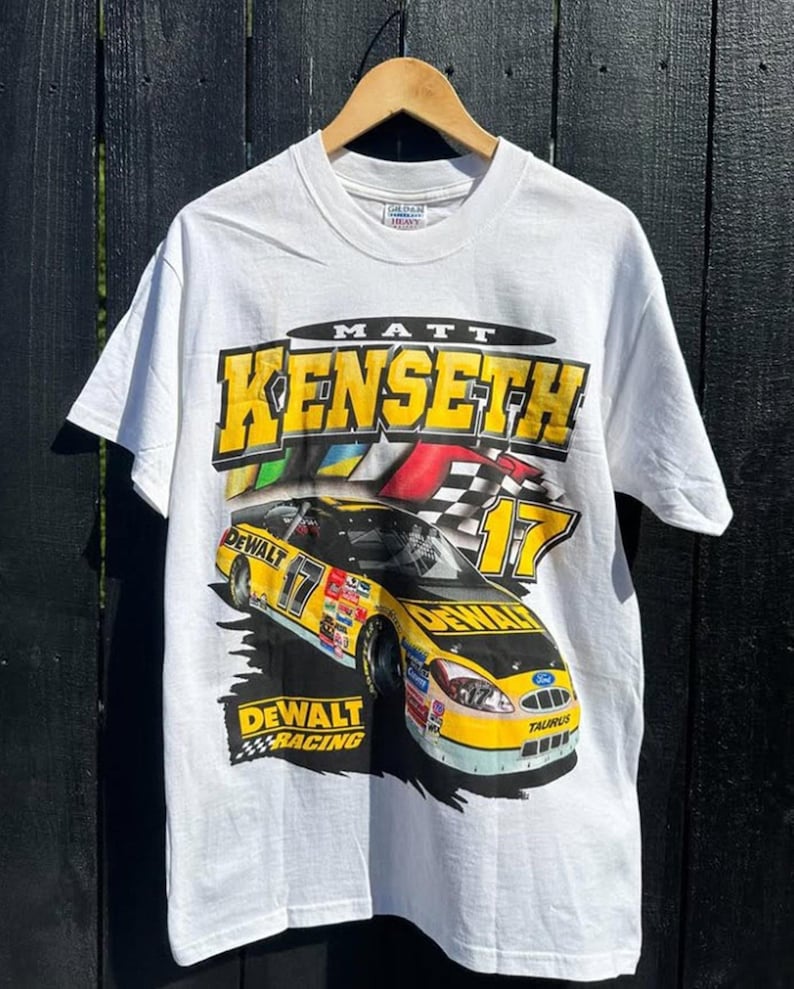 May include: White t-shirt with a yellow and black race car graphic. The car has the number 17 and the text "DEWALT RACING" on it. The text "MATT KENSETH" is above the car.