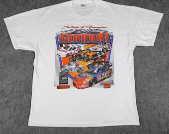 May include: White t-shirt with a colorful graphic of race cars and the text "Salute to Champion Jeff Gordon Knoxville Iowa".