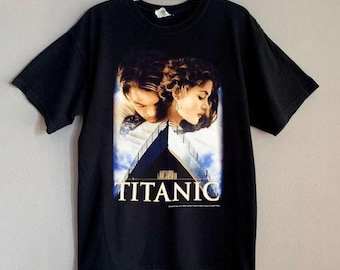 May include: Black t-shirt featuring a movie poster graphic. The graphic depicts two people with the word "TITANIC" in white block letters. The image has a blue and white background.
