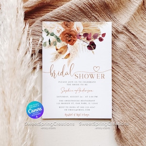 May include: Bridal shower invitation with a floral design in rust, cream, and burgundy. The invitation includes the text "bridal shower" and event details. The background features a beige fabric and pampas grass.