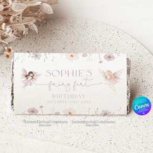 May include: A white chocolate bar wrapper with a floral design and pink fairies. The text reads "Sophie's fairy first birthday December 24th 20XX".
