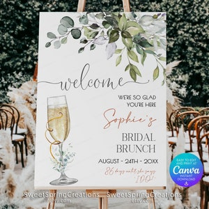 Könnte beinhalten: Ein Willkommens-Schild für einen Braut-Brunch mit einem Aquarell-Design aus Grünpflanzen und einer Champagnerflöte. Das Schild lautet "Willkommen, wir freuen uns, dass Sie da sind, Sophies Braut-Brunch, August 24., 20XX, 86 Tage bis sie Ja sagt!" und enthält ein Canva-Logo.