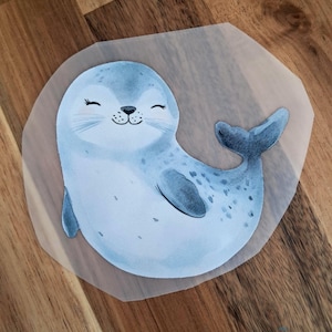 Könnte beinhalten: Illustration eines hellblauen Cartoon-Seehunds mit fröhlichem Gesichtsausdruck. Der Seehund hat dunkelblaue Flecken und einen dunkelblauen Schwanz. Die Illustration befindet sich auf transparentem Hintergrund.