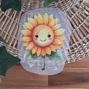 Könnte beinhalten: Eine fröhliche gelbe Sonnenblume mit einem lächelnden Gesicht, im Aquarell-Stil gemalt. Die Sonnenblume hat grüne Blätter und einen Stiel und ist von weißen Punkten auf einem hellgrauen Hintergrund umgeben.