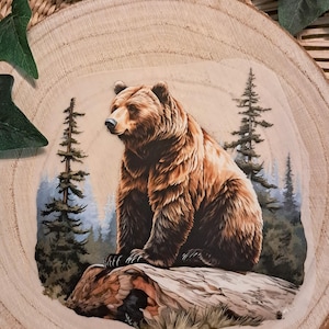 Könnte beinhalten: Illustration eines braunen Bären auf einem Baumstamm, mit einem Wald im Hintergrund. Das Bild ist auf einer natürlichen Holzscheibe dargestellt und erzeugt eine rustikale Ästhetik. Thema: Natur und Wildtiere.