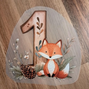 Könnte beinhalten: Eine verspielte Illustration mit einem Fuchs und der Zahl 1. Der Fuchs ist orange und weiß, umgeben von Grün und einem Tannenzapfen. Die Zahl 1 ist braun mit Blättern, perfekt für den ersten Geburtstag.