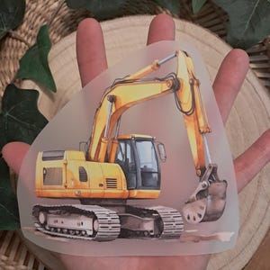 Könnte beinhalten: Ein durchscheinender Aufkleber mit einer detaillierten Illustration eines gelben Hydraulikbaggers mit schwarzer Kabine, Metallketten und einer großen Baggerschaufel. Das Baufahrzeug ist in einer Seitenansicht mit realistischer Schattierung dargestellt.