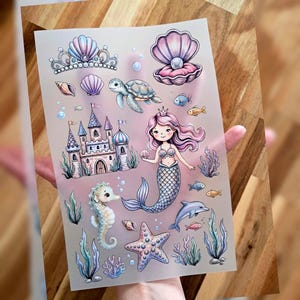Könnte beinhalten: Ein Bogen mit Aufklebern zum Thema Meerjungfrau, mit einer Meerjungfrau, einem Schloss, einem Seepferdchen, einem Seestern, einem Delfin und anderen Meereskreaturen. Die Aufkleber sind in Rosa-, Blau- und Lilatönen gehalten und haben ein perlmuttartiges Finish.