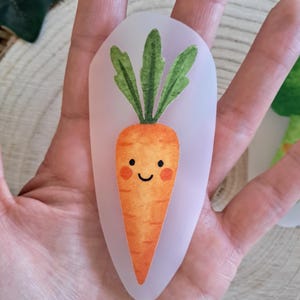 Könnte beinhalten: Ein skurriler Karottenaufkleber mit einem lächelnden Gesicht, einem orangefarbenen Körper und einem grünen, blattartigen Oberteil. Der Aufkleber befindet sich auf einem durchscheinenden Hintergrund. Das Karottendesign ist eine niedliche, verspielte Illustration.