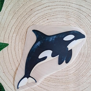 Könnte beinhalten: Ein Holzstempel mit einem stilisierten Orca-Wal-Design in Schwarz und Weiß. Der Orca ist mit detaillierten Konturen dargestellt. Der Stempel befindet sich auf einem hellen Holzgrund mit sichtbarer Holzmaserung.