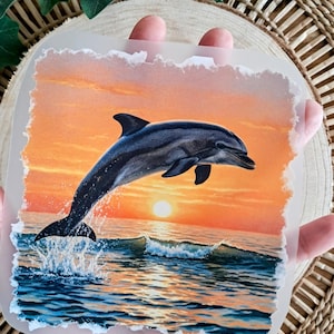 Könnte beinhalten: Quadratisches Bild eines Delfins, der bei Sonnenuntergang aus dem Meer springt. Der Delfin ist dunkelgrau, das Wasser blau mit weißen Wellen und der Himmel orange und gelb.