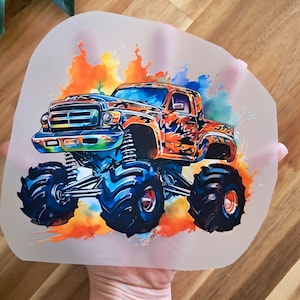 Könnte beinhalten: Eine farbenfrohe Illustration eines Monstertrucks mit großen blauen Reifen und orangefarbenen und blauen Akzenten. Der Truck ist vor einem lebendigen Aquarell-Spritzer aus Orange, Blau und Gelb platziert.