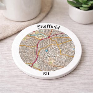 May include: A white ceramic coaster featuring a detailed map of Sheffield, England. The city name is printed in black at the top, with the postcode S11 at the bottom. The map shows streets, parks, and landmarks.
