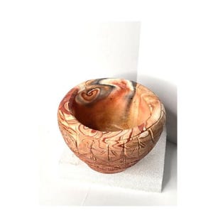 May include: A handcrafted, round bowl with a unique marbled design in shades of brown, orange, and cream. The exterior features a textured, carved pattern. This decorative bowl is suitable for various uses.